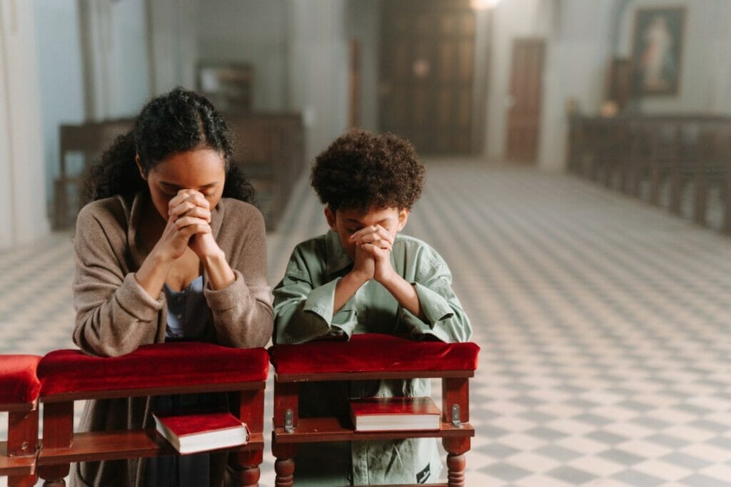 A serene and tender moment captured within the walls of a peaceful church. A devoted woman, accompanied by her child, sits in a pew, heads bowed in prayer. The soft light from the stained glass windows bathes them in a gentle, comforting glow. Together, they seek solace and offer their heartfelt prayers, a touching scene of faith and gratitude after surgery.