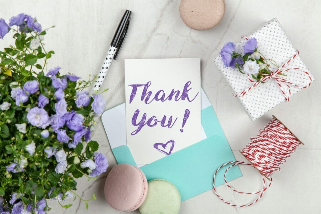 Expressing gratitude with elegance: A 'Thank you note to parents for teacher appreciation gift' beautifully displayed on a pristine white background, accompanied by vibrant flowers and a carefully wrapped gift package.