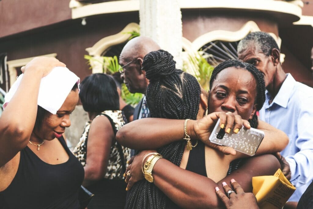 A somber scene at a funeral prayer gathering with many humans. One woman, overwhelmed by grief, is consoled by every other girl who embraces her, exemplifying empathy. what are the components of empathy
