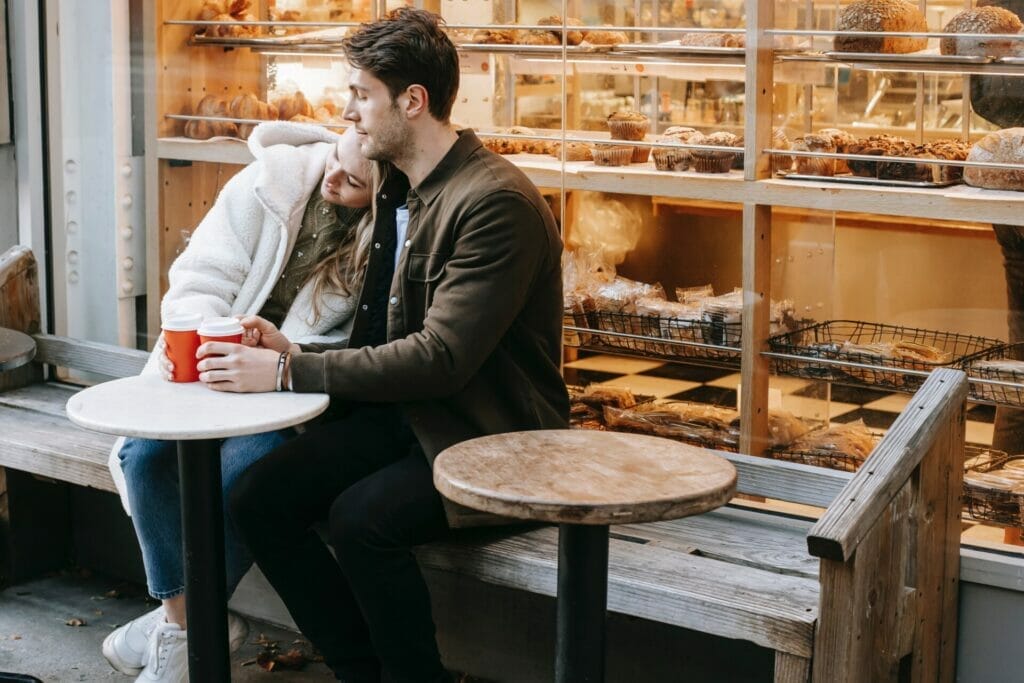A couple sitting in a comfy espresso shop, with the lady leaning her head at the boy's shoulder, carrying out small communication and enjoying a heartfelt communication.
